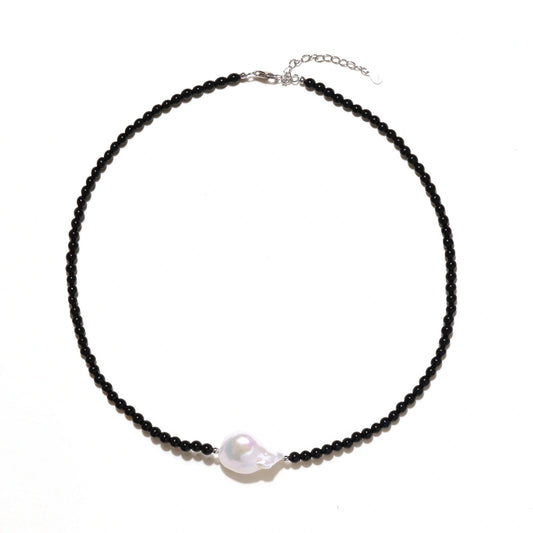 Beaded black agate necklace with iridescent baroque freshwater pearl centerpiece on cream background.