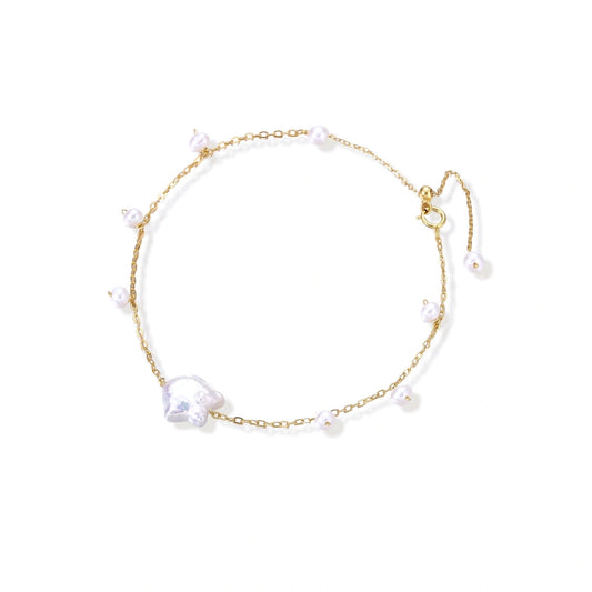 Delicate gold chain bracelet with baroque pearl centerpiece and small freshwater pearls on cream background.