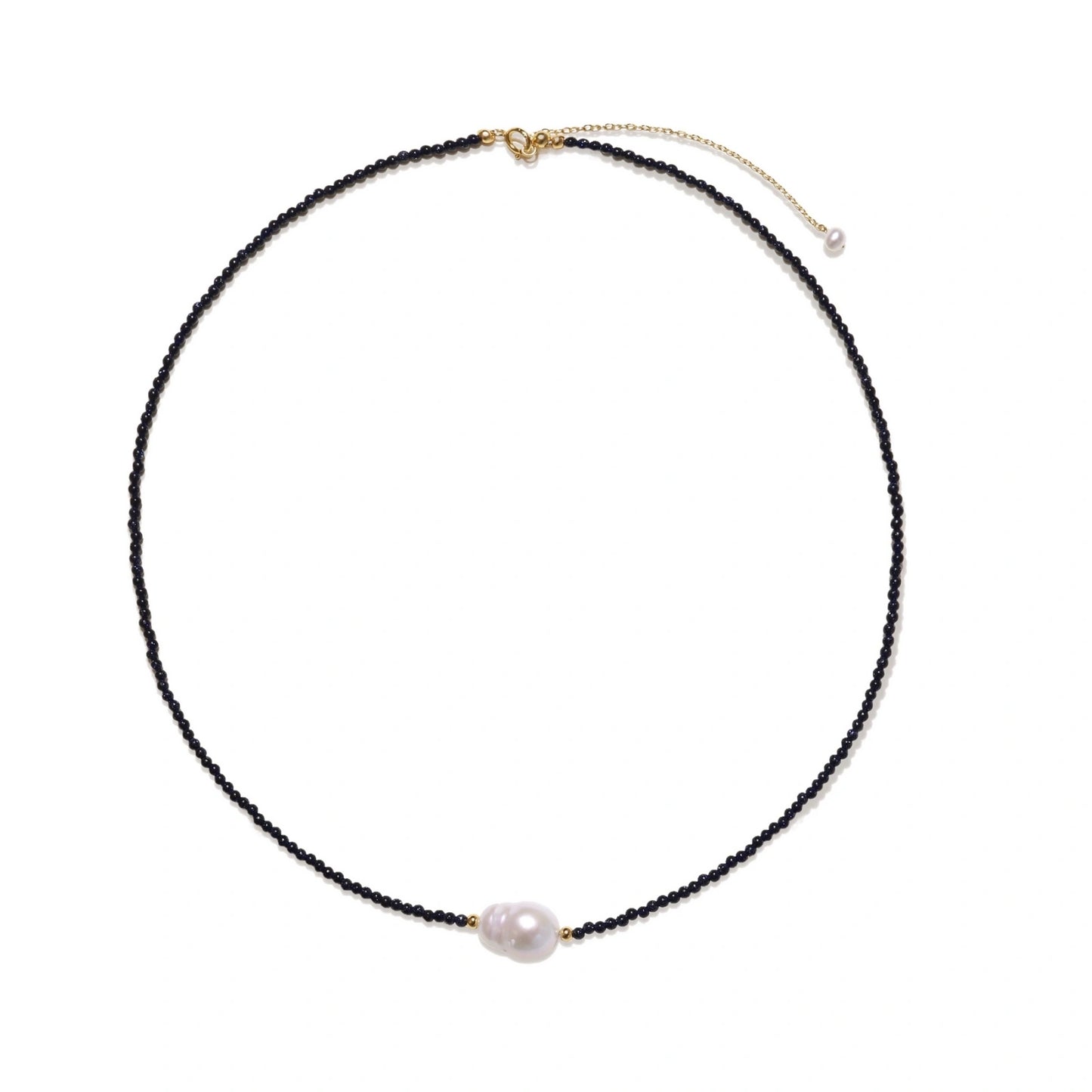 Delicate necklace with black blue sandstone beads and baroque pearl center on white background with gold accents.