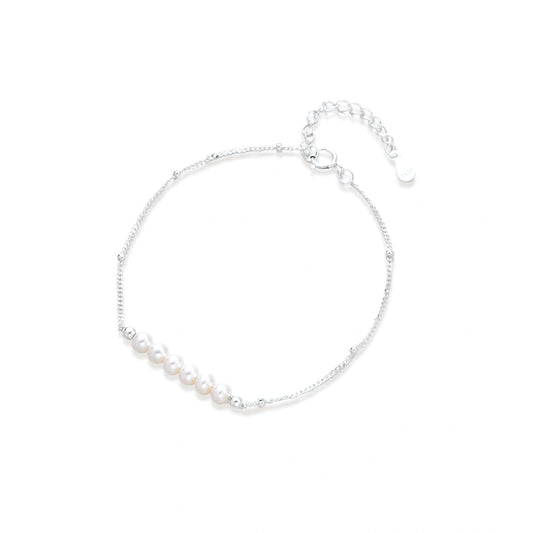 Delicate rhodium-plated silver chain bracelet with row of small baroque pearls centered on white background.