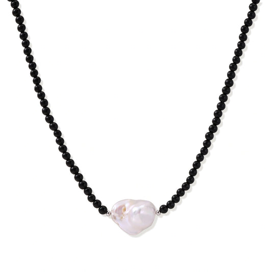 Beaded black agate necklace with iridescent baroque freshwater pearl centerpiece on cream background.