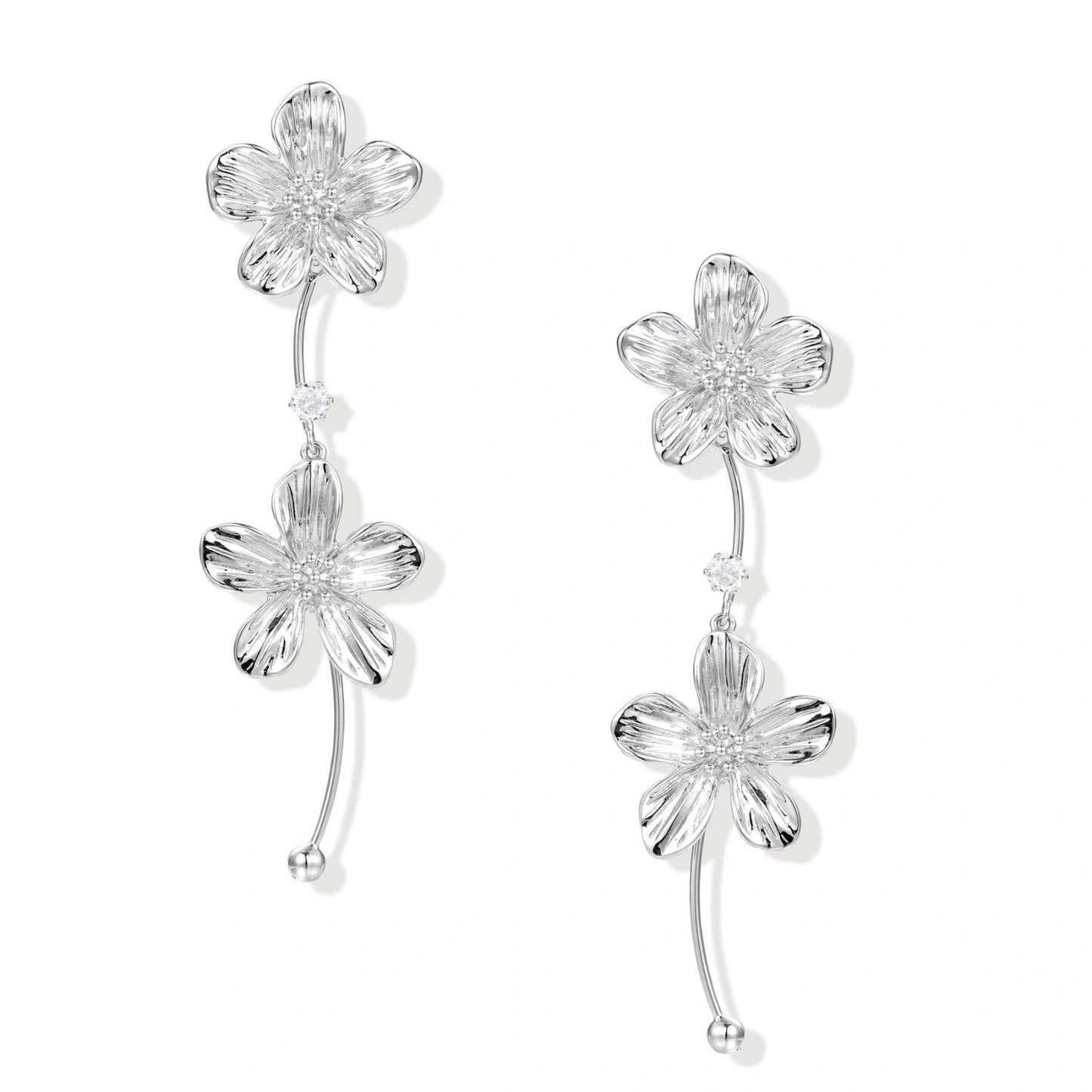 Silver-white asymmetric earrings with textured flower petals and crystal centers on cream background