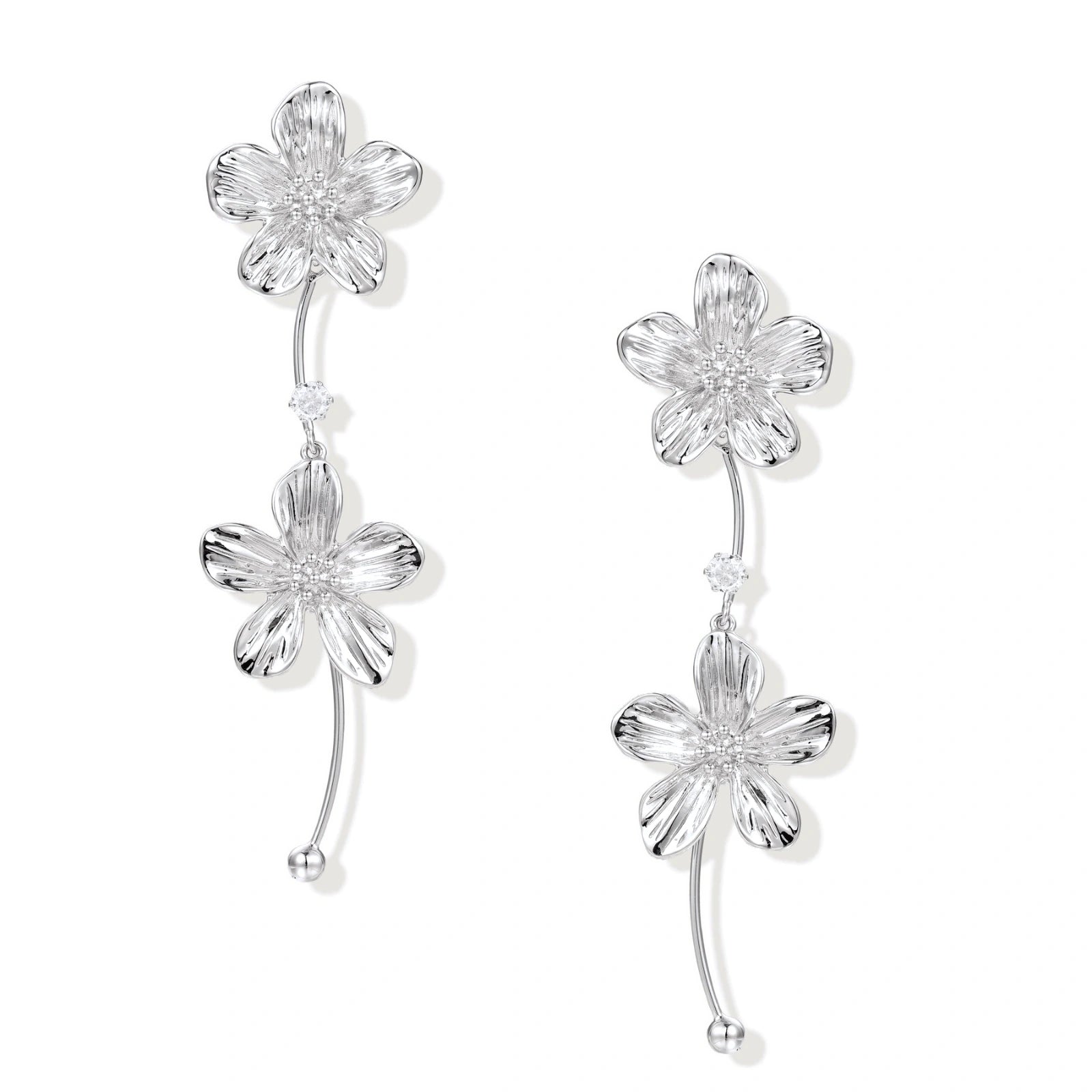 Silver-white asymmetric earrings with textured flower petals and crystal centers on cream background