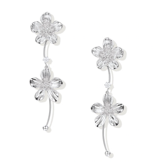Silver-white asymmetric earrings with textured flower petals and crystal centers on cream background